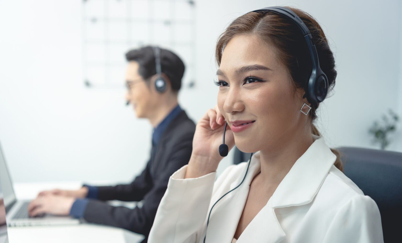 Asian call center agent team, customer service support wearing headset or headphone talking with customer in modern office.